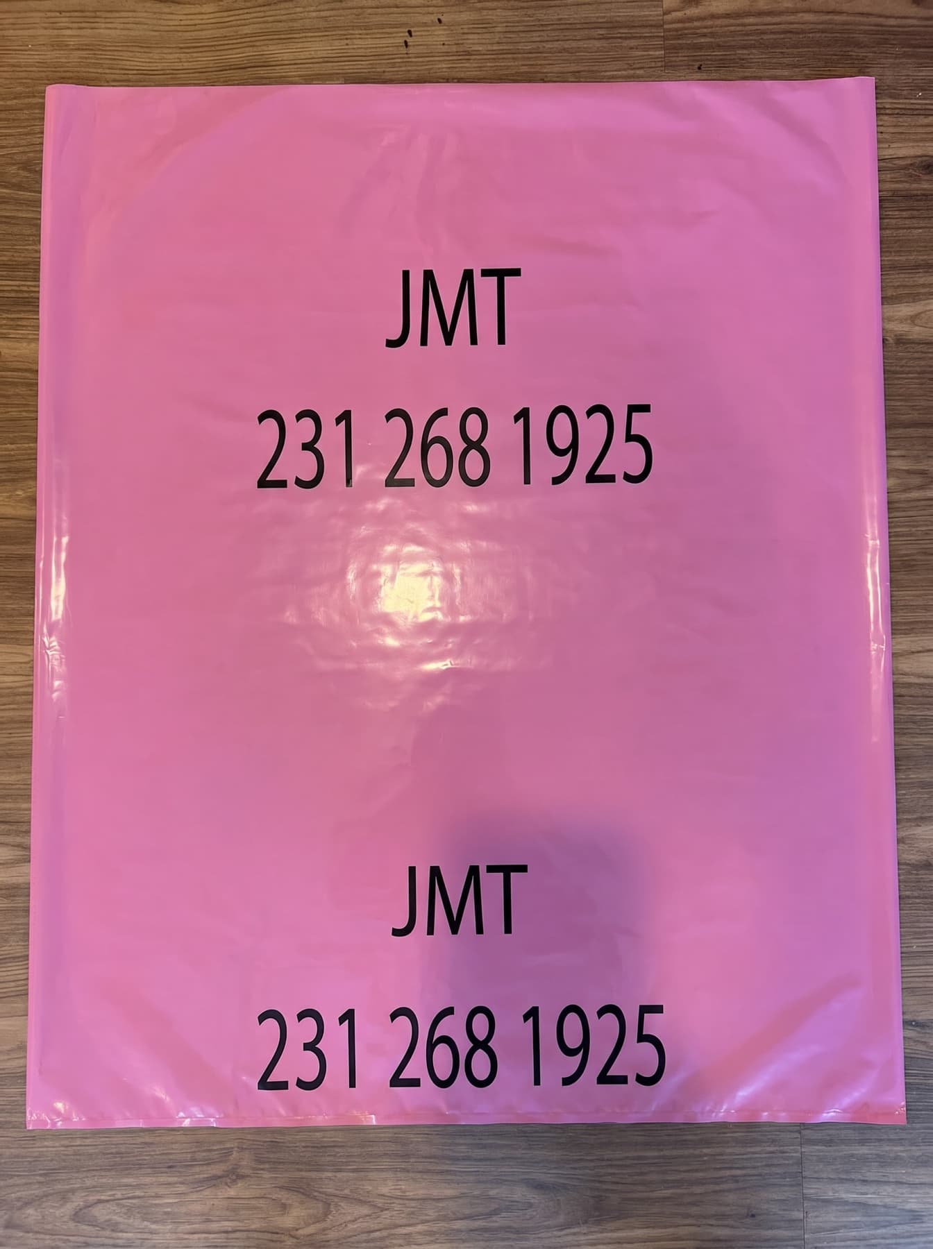 JMT pink trash bag laid flat showing the JMT logo and phone number 231 268 1925 printed in black — the same bag sold at local retailers.