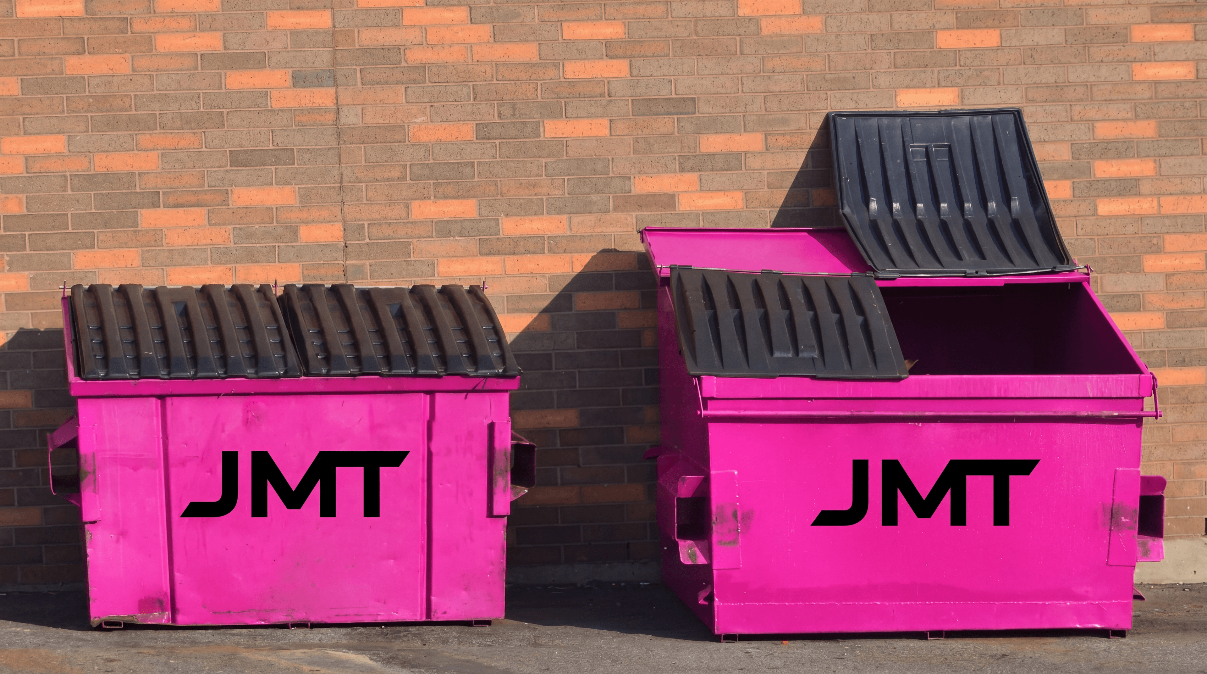 A pair of JMT-branded pink dumpsters against a brick wall.